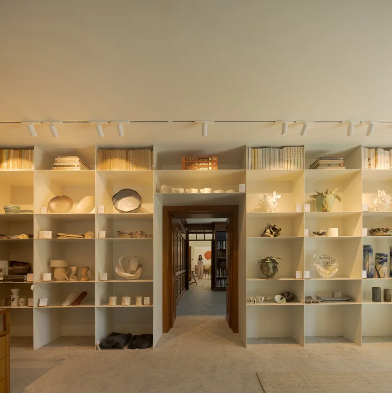 White shelving grid displaying ceramics and objects with a timber doorway framing a corridor beyond