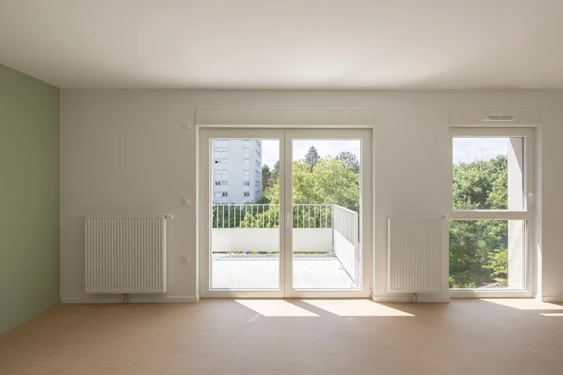 Bare interior room with pale wood flooring, wall-mounted radiators and sliding door to exterior balcony