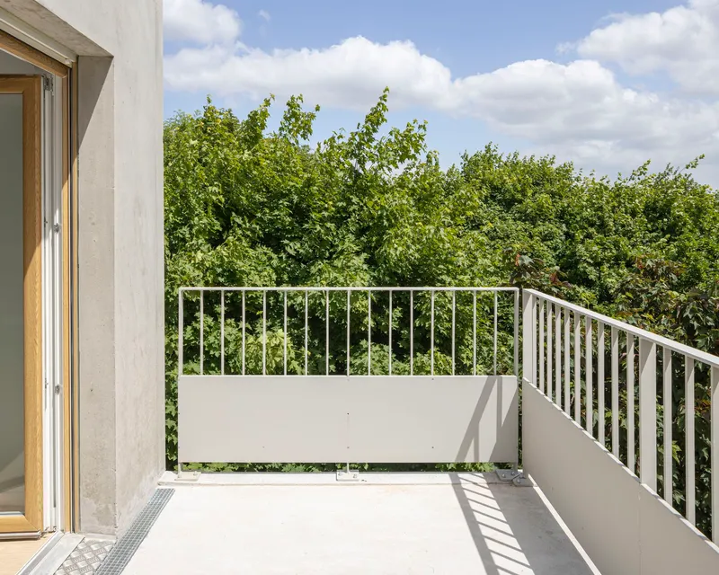 White balcony with metal railings overlooking dense green foliage under a partly cloudy sky