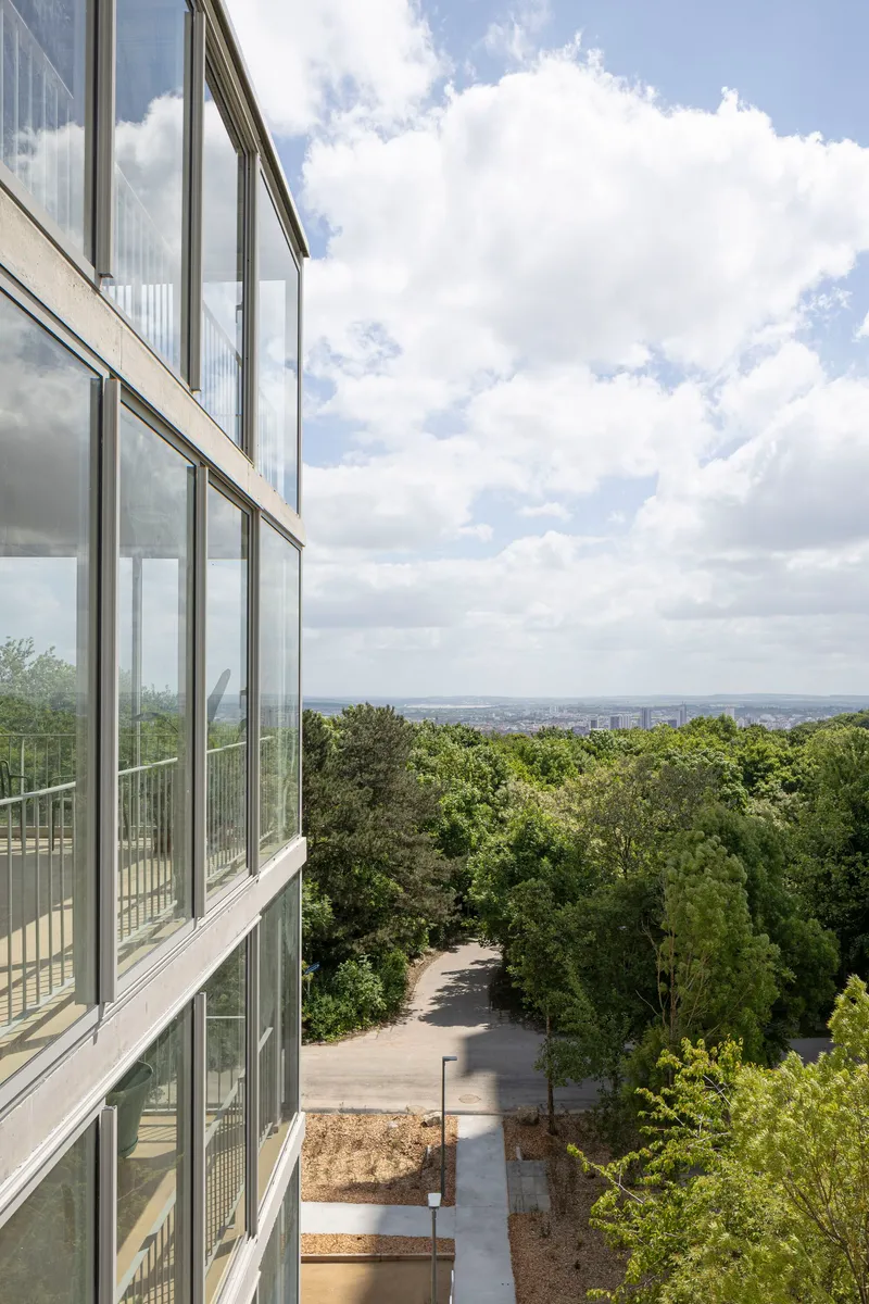 Glazed facade with metal mullions overlooking terraced landscape and distant horizon under cloudy sky