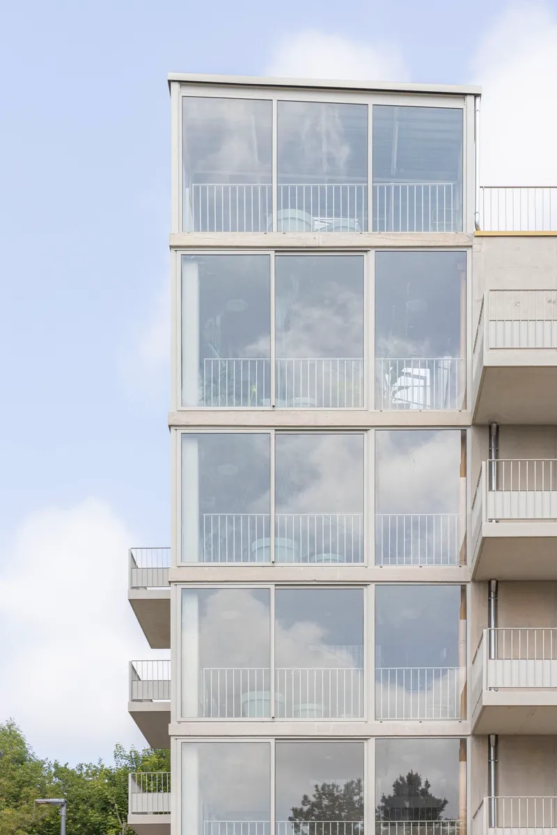 Stacked glazed balconies with white metal railings rising against a cloudy sky