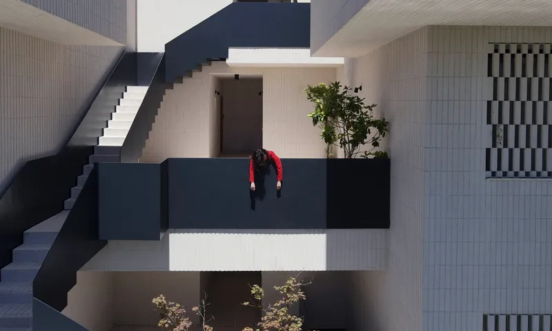 Overhead view of a figure in red leaning over the black steel railing of a courtyard bridge