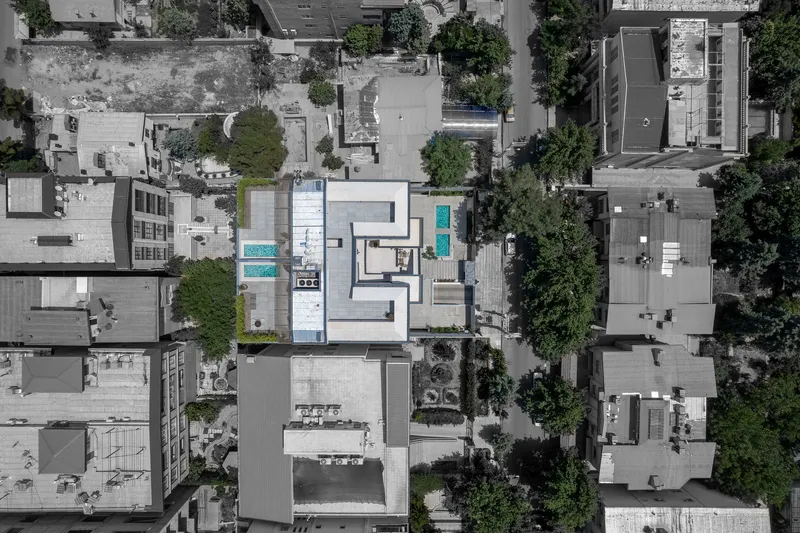 Aerial view showing the building's stacked white volumes with rooftop pools amid surrounding urban fabric