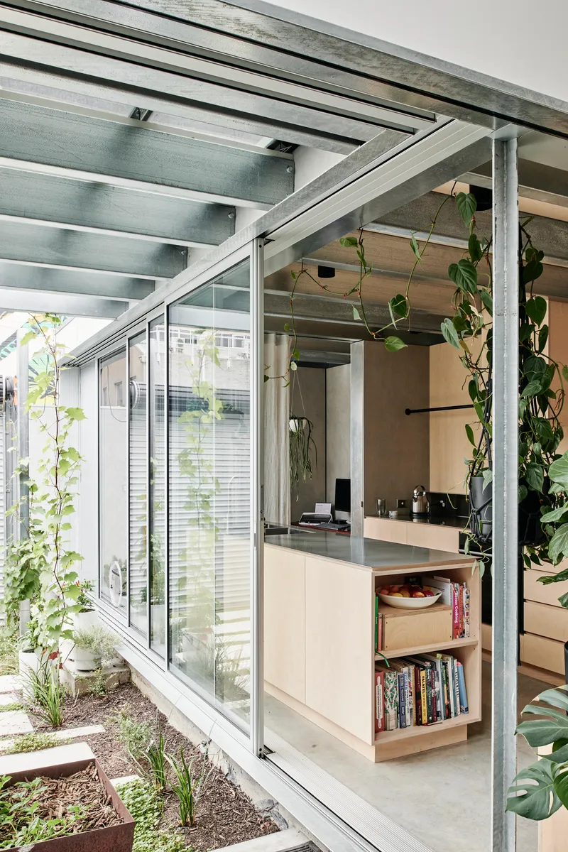 Kitchen island under exposed steel beams with climbing vines framing the glazed courtyard beyond