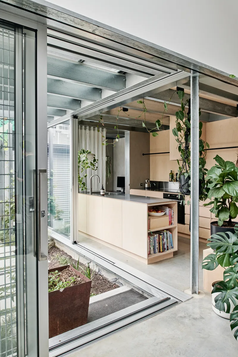 Open sliding glass doors revealing the kitchen and steel structural frame with hanging plants