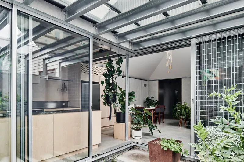 Interior looking through the glazed steel structure connecting kitchen and dining spaces with planted courtyard
