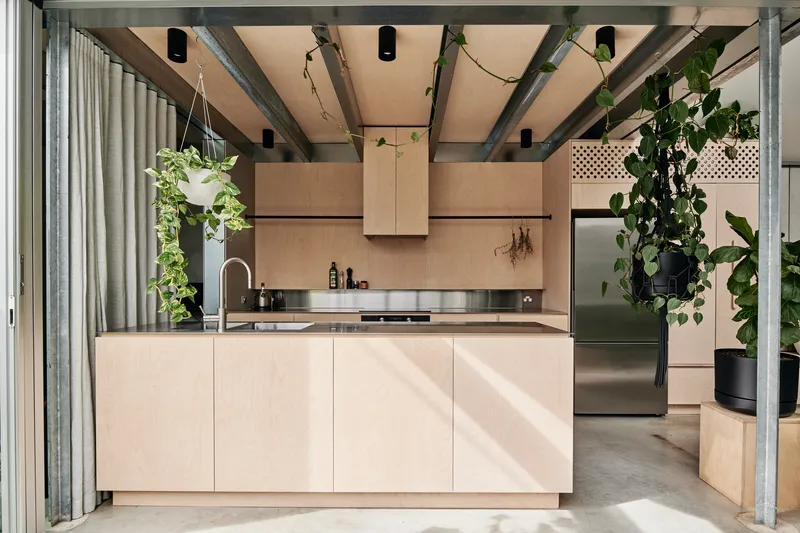 Plywood kitchen island with stainless steel countertop under exposed steel beams and pendant lights
