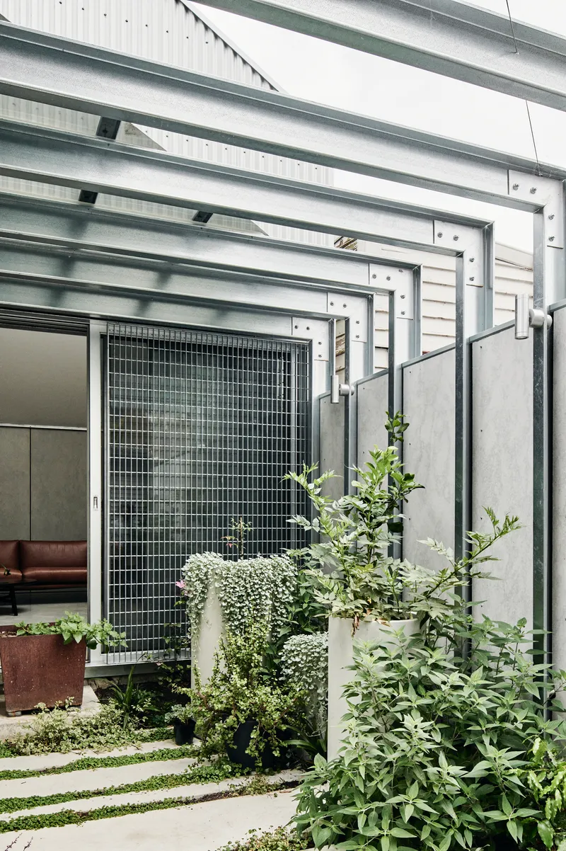 Planted courtyard with grass pavers and wire mesh screen framed by steel overhead beams