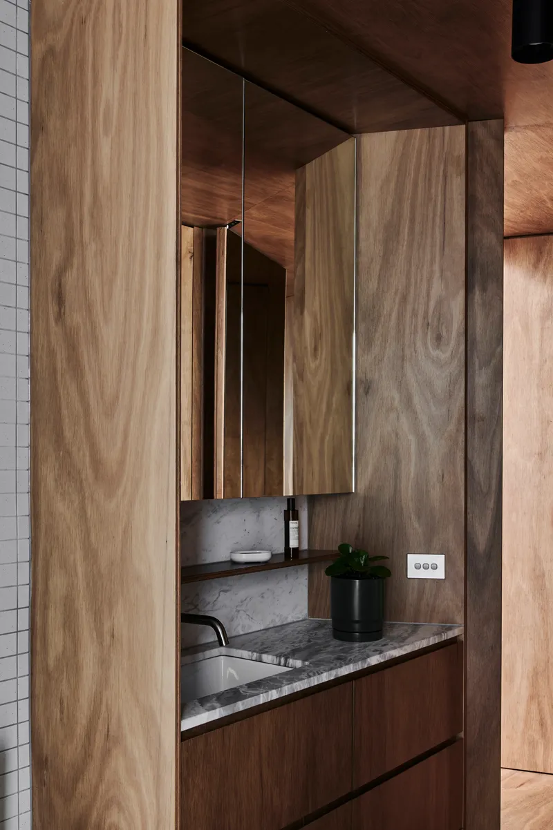 Bathroom vanity with timber cabinetry and marble countertop set within mirrored niche