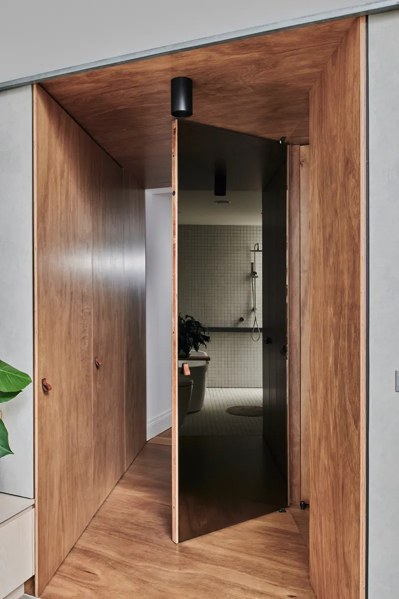 Walnut timber hallway with pivoting door revealing tiled bathroom beyond