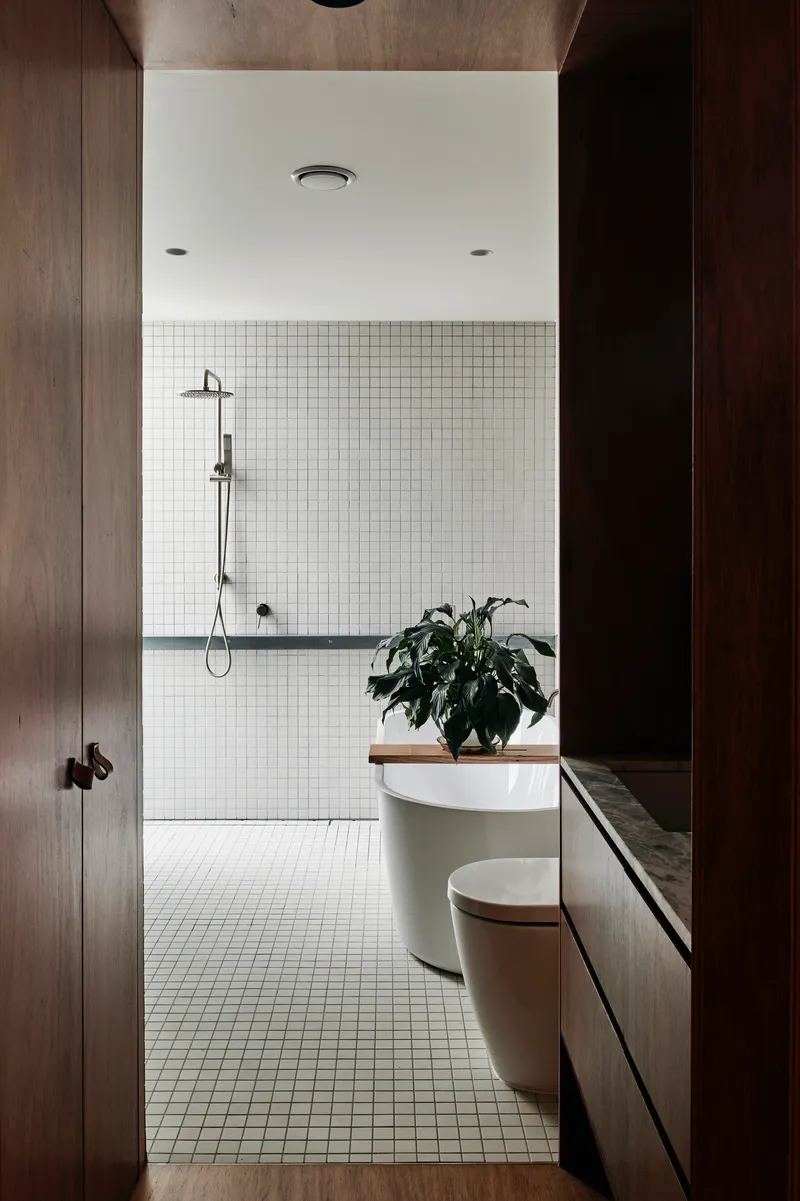 Bathroom with white mosaic tile walls, freestanding tub, and timber vanity under potted plant
