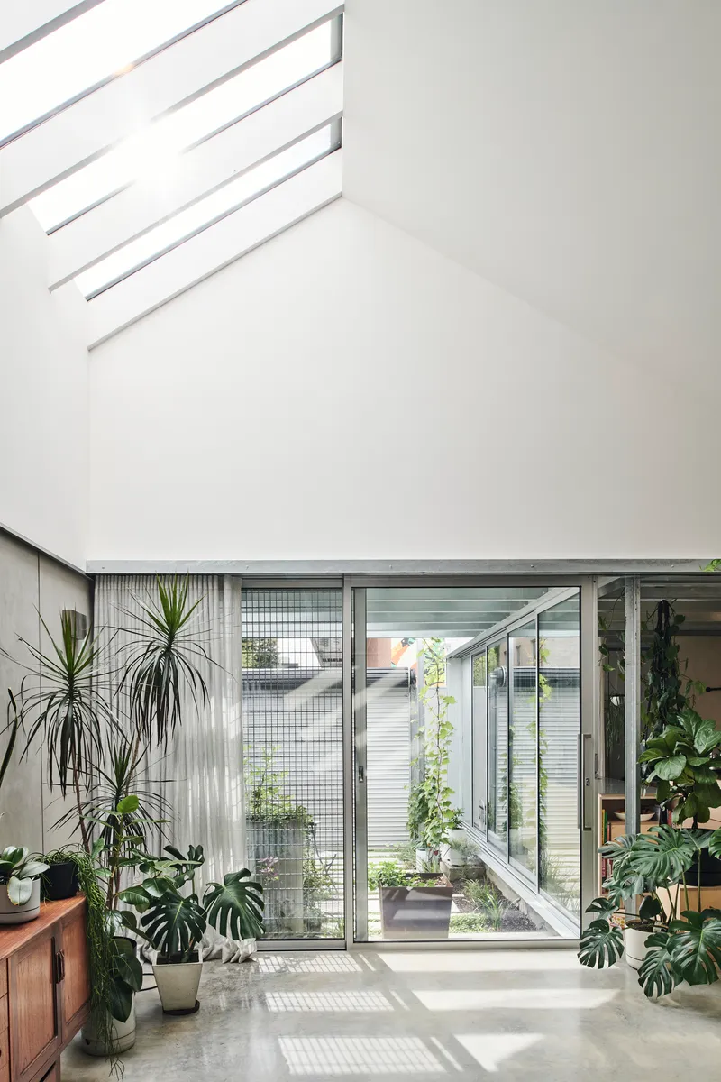 Double-height atrium space with glazed walls opening onto a tiled courtyard filled with potted plants
