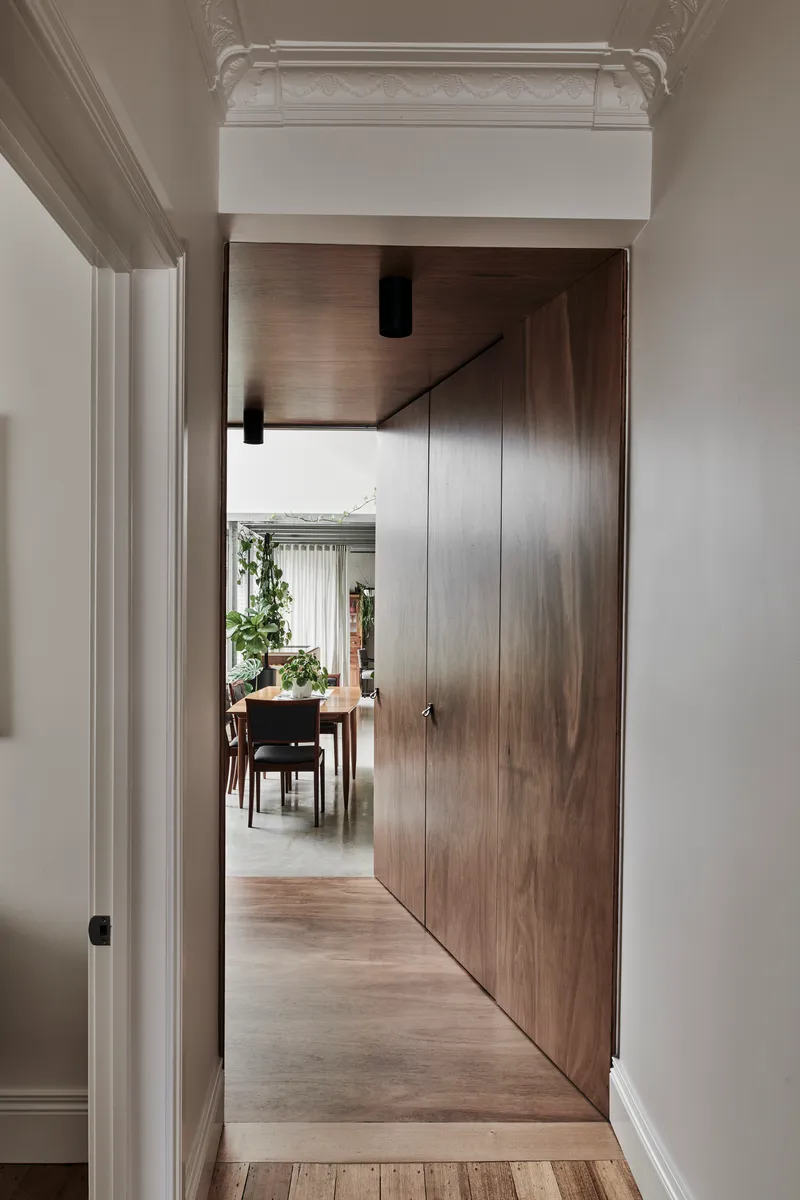 Timber veneer pivot door framed by white plaster walls with ornate ceiling molding visible above