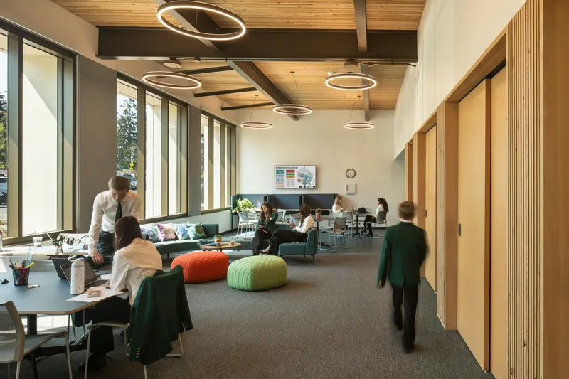 Interior lounge with timber ceiling panels, circular ring pendants, and floor-to-ceiling windows along one wall