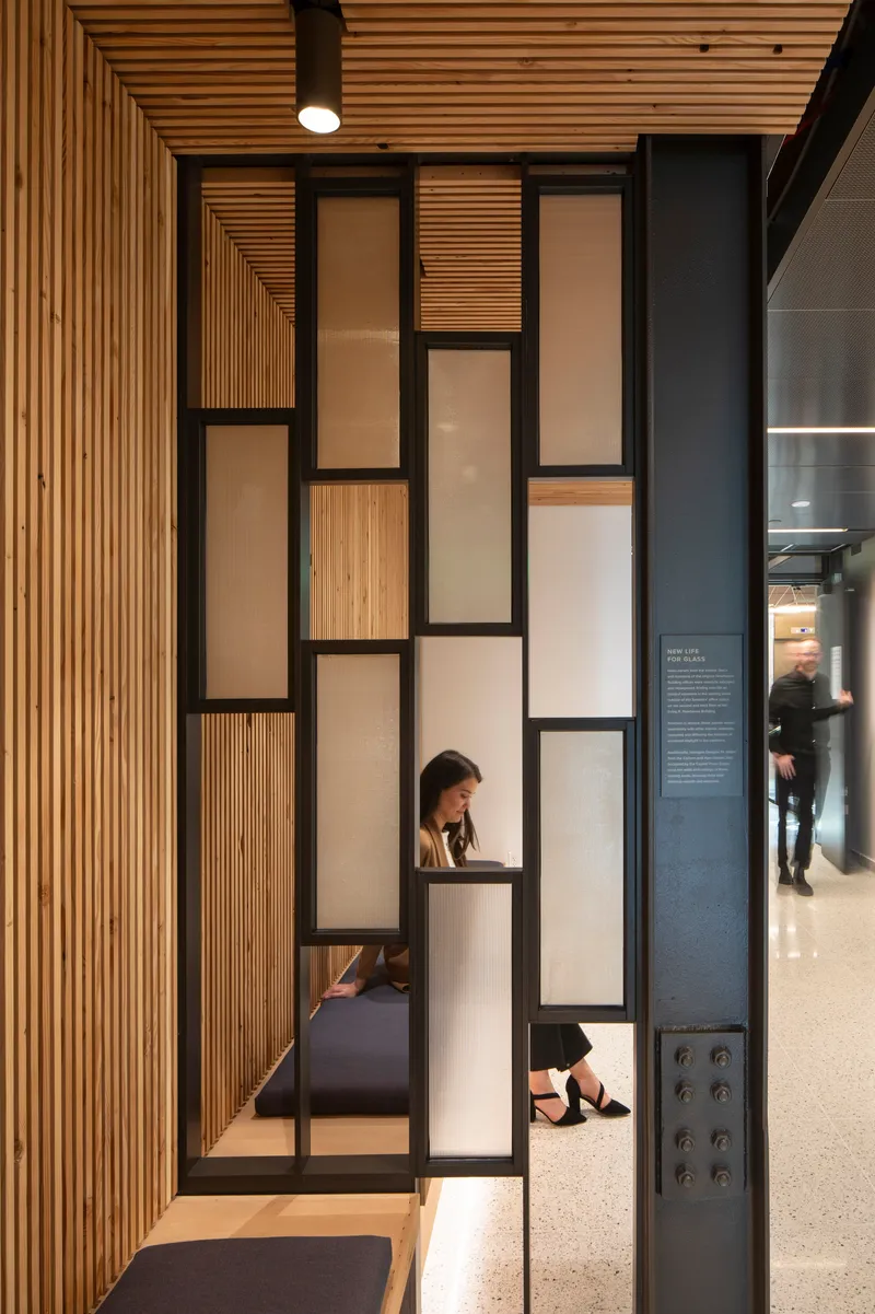 Black steel frame partition with alternating timber and frosted glass panels beside timber slat wall