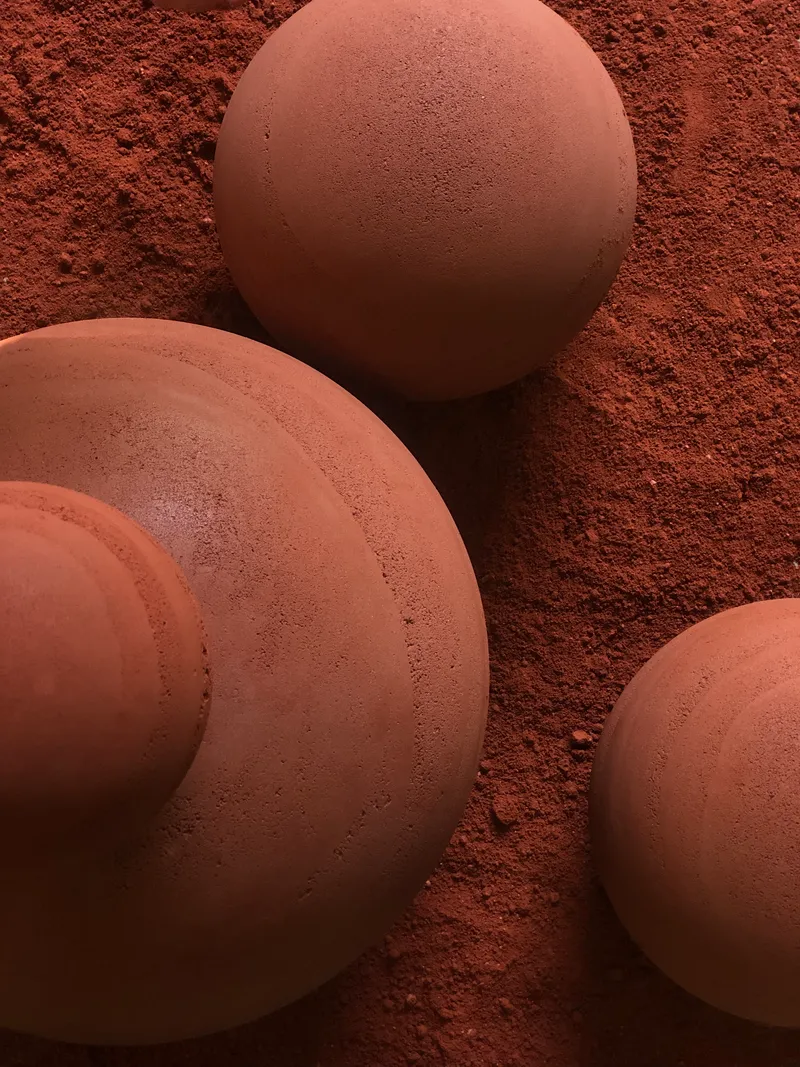 Close-up of textured terracotta spheres meeting red soil showing surface seams and grain