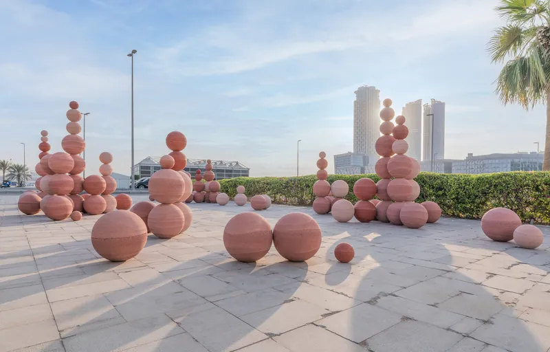 Arrangement of earthen spheres on a rooftop plaza with distant towers and palm trees