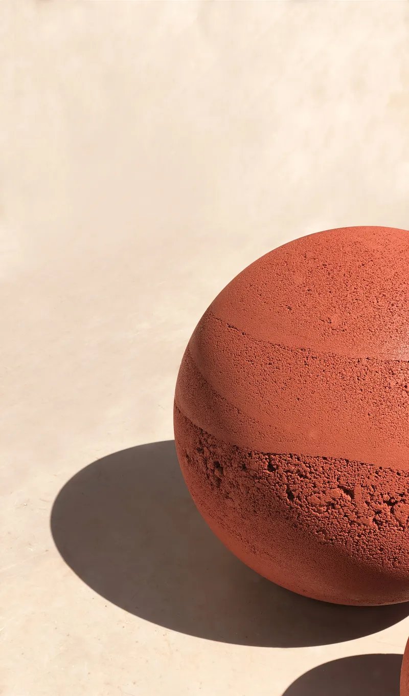 Single terracotta sphere on white concrete casting a hard shadow in daylight