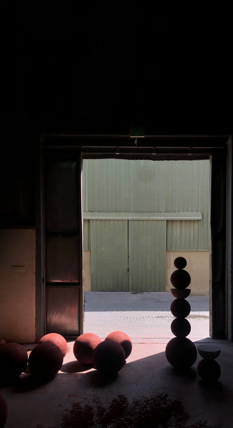 Doorway framing stacked spherical sculptures in shadow with sunlit courtyard and green metal doors beyond