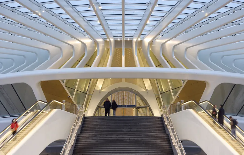 Escalator rising beneath the layered white ceiling ribs and glass skylight with passengers descending