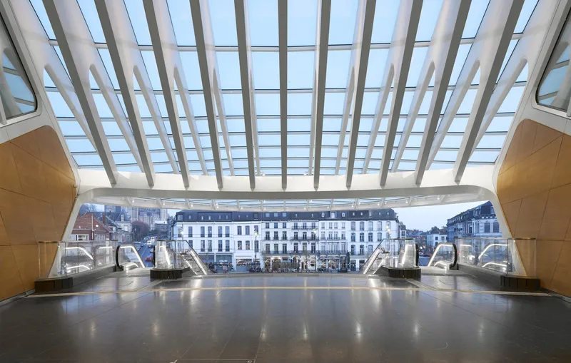 Station concourse with white steel and glass canopy framing historic buildings beyond escalators