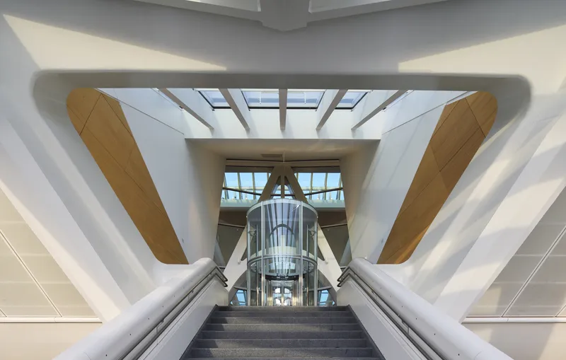 Central staircase flanked by white angular structural ribs and timber-clad columns under skylights
