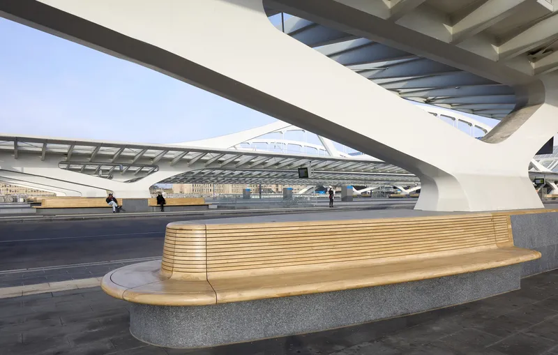 Curved timber bench with granite base on platform under white steel canopy ribs