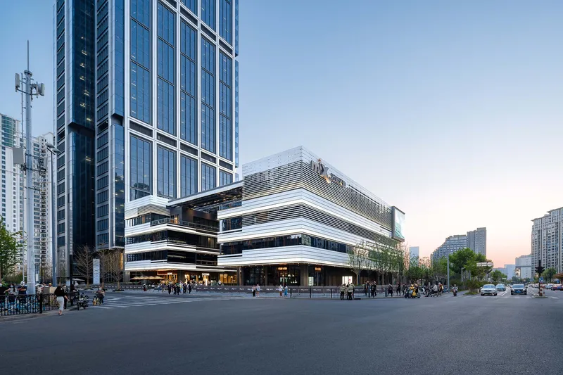 Street-level view of horizontal banded facade with deep overhangs at dusk beside a glass tower