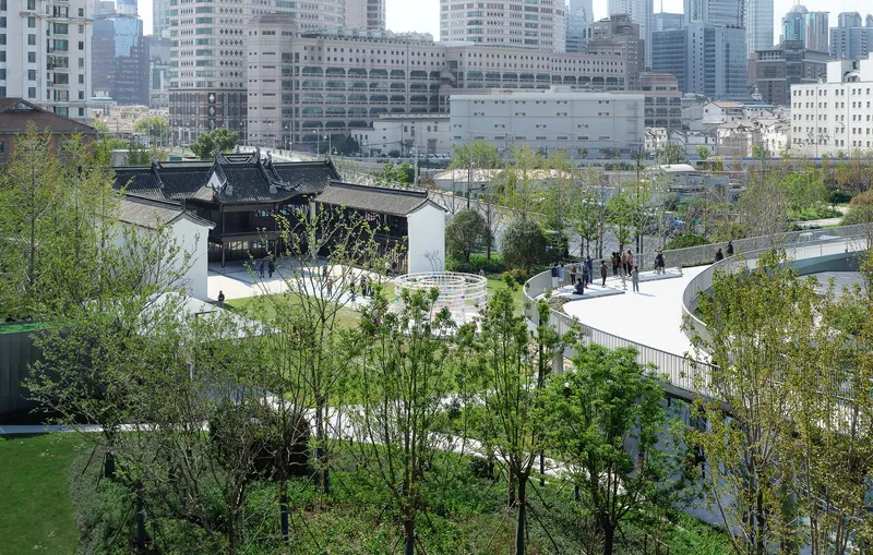 Elevated view of traditional pavilion with black-tiled roof set within terraced landscape and young trees