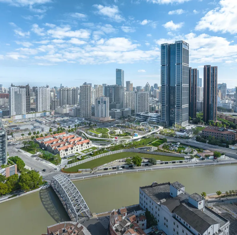 Aerial view of a landscaped park with curving pathways along a river under partly cloudy skies