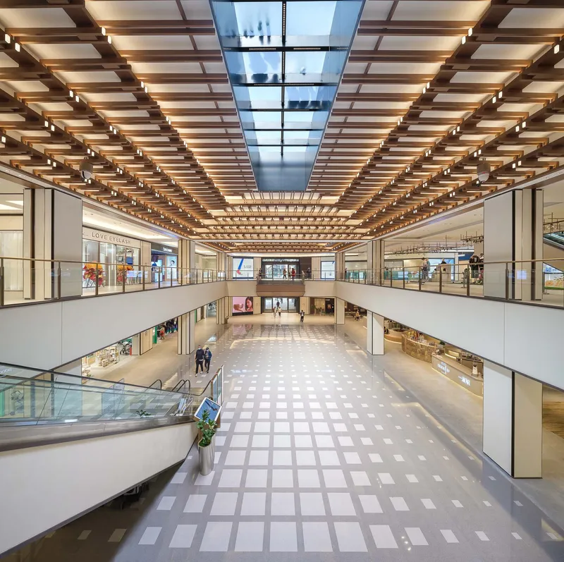 Multi-level atrium with gridded skylight and timber slat ceiling above balconies and storefronts