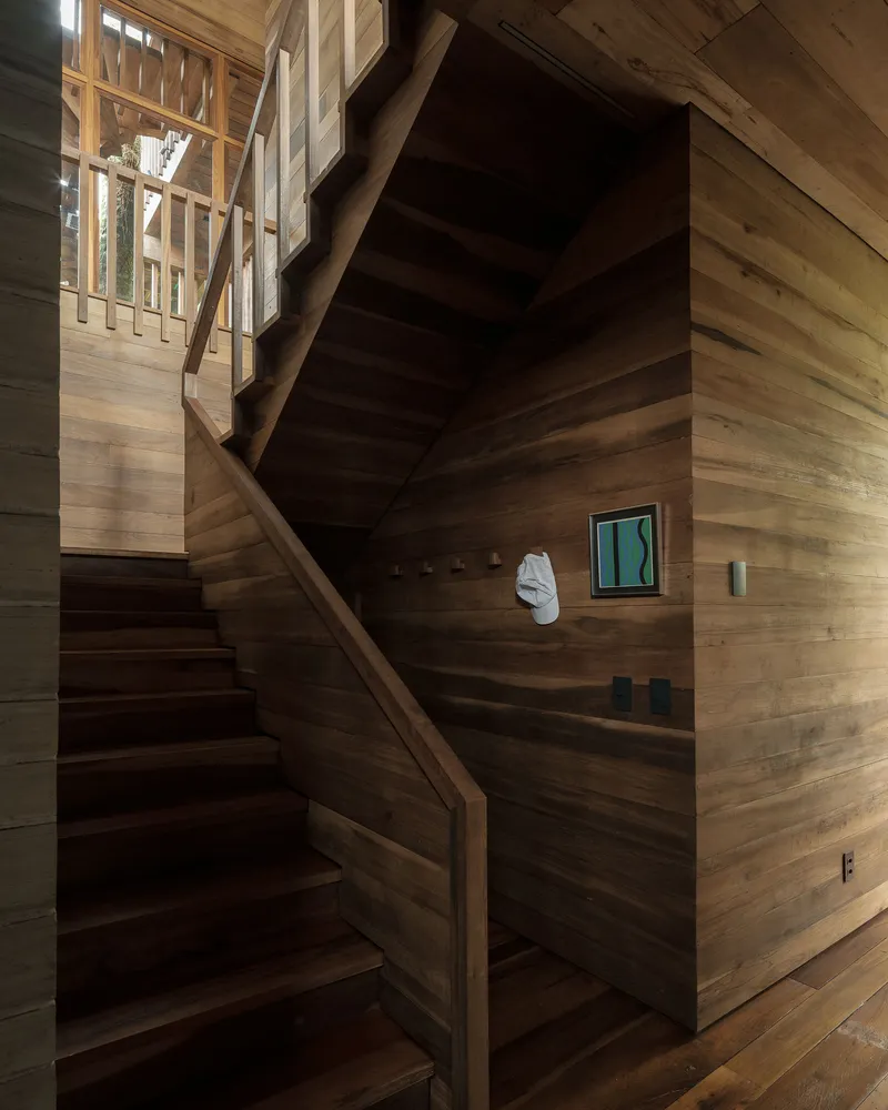 Timber staircase wrapping around walls clad in horizontal wood planks with a small window above