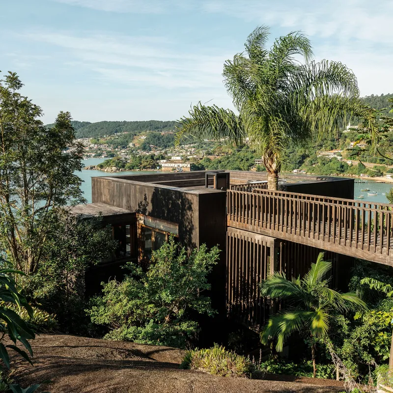 Timber-clad residence with vertical slat screen perched on hillside above coastal bay and palm trees