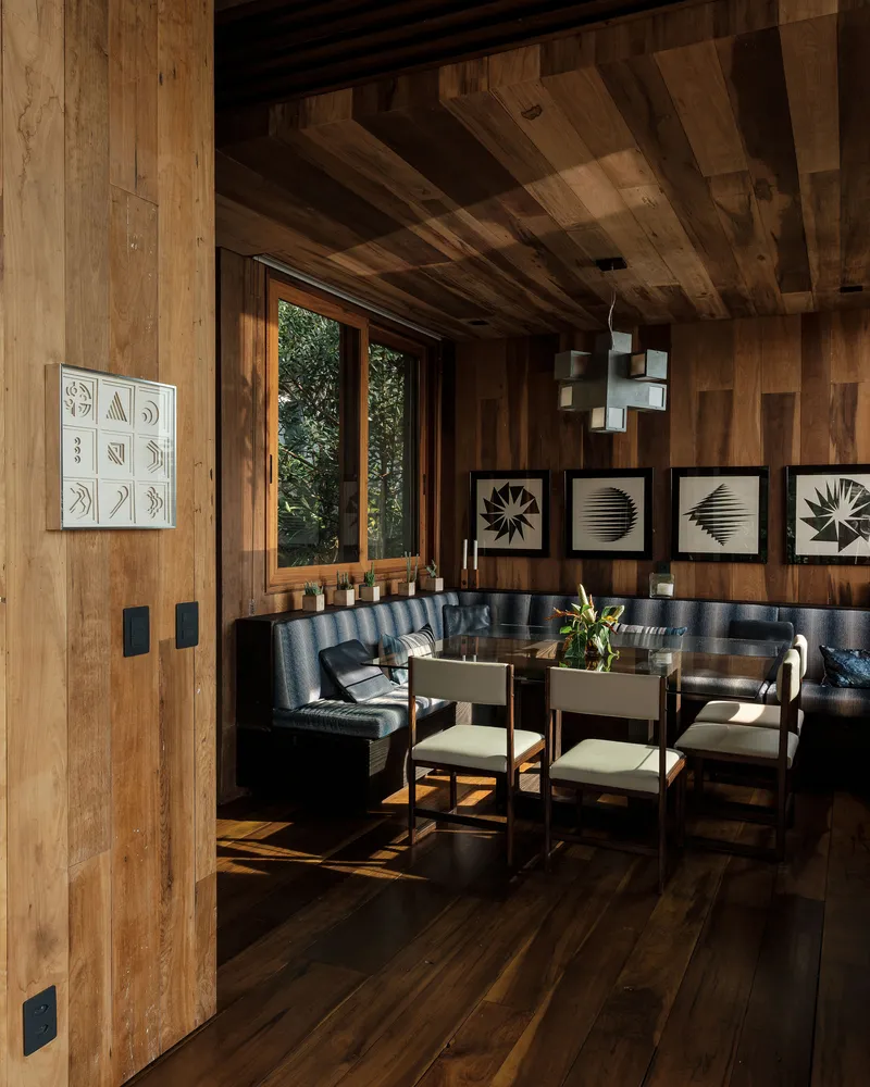 Wood-paneled dining area with exposed timber ceiling beams and built-in banquette seating beneath framed botanical prints
