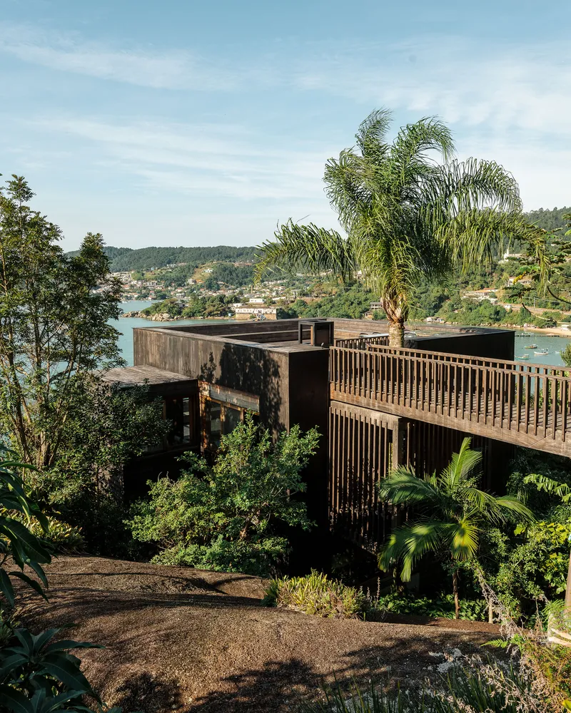 Terraced timber structure with slatted screen balcony rising above dense vegetation on the hillside