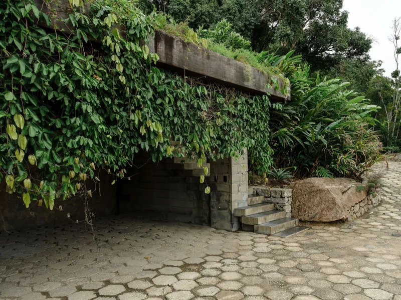 Concrete overhang draped with vines above hexagonal paving stones and a boulder at dusk