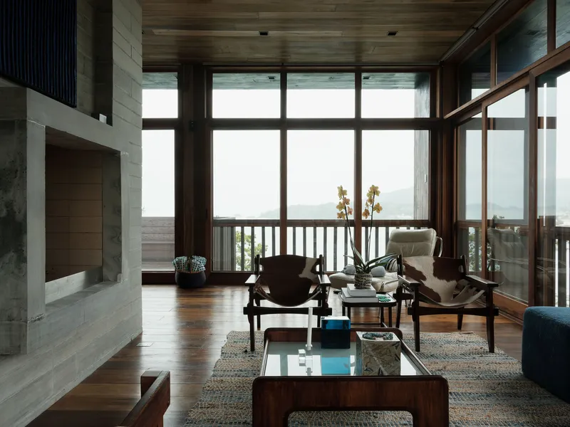 Living room with concrete fireplace and timber ceiling framing a view of distant hills