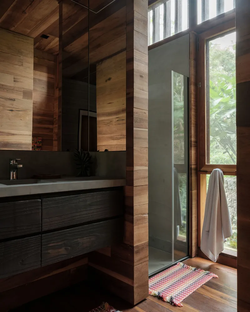 Bathroom with timber plank walls, dark vanity and tall glazed door opening to garden
