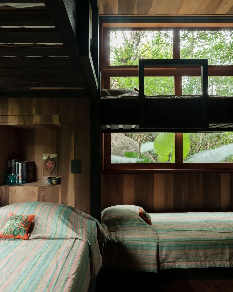 Bedroom with timber-lined walls and staggered horizontal windows framing views of tropical foliage