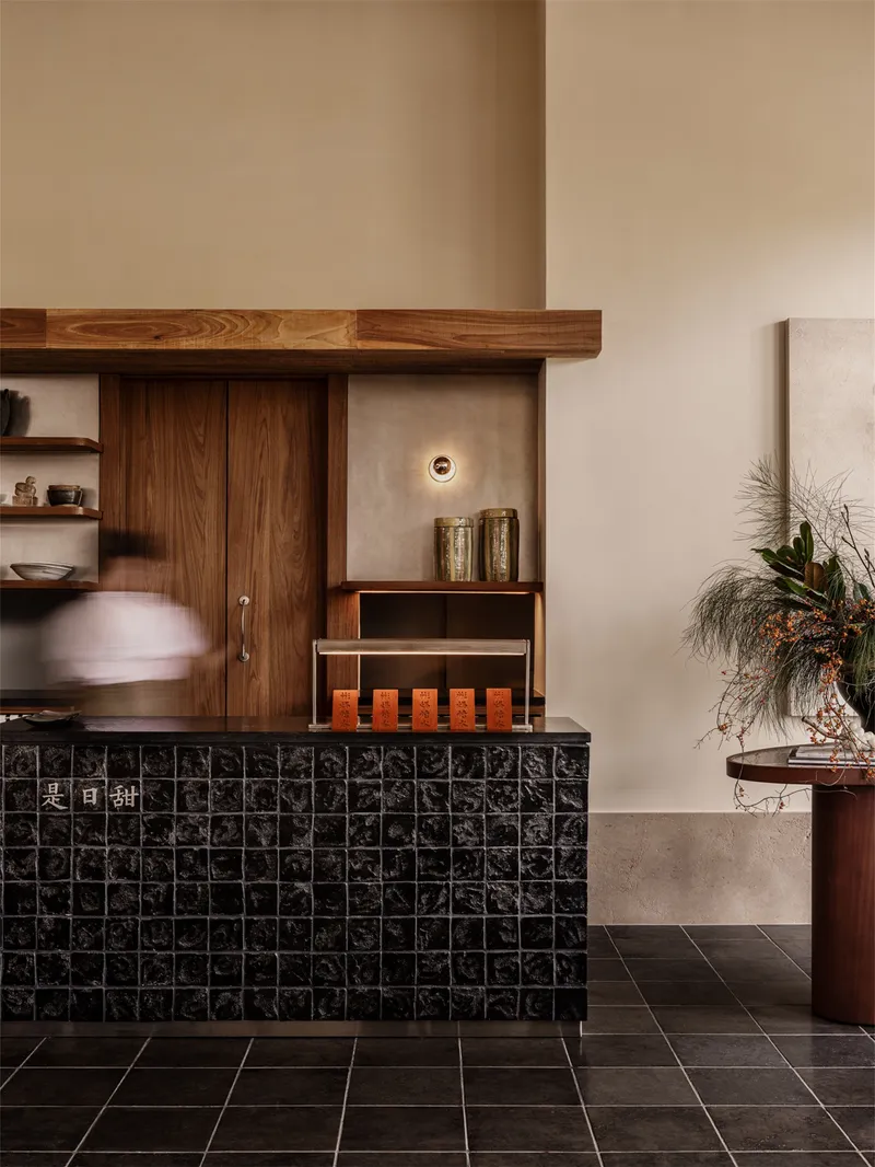Black glazed tile counter fronting timber millwork wall with sliding doors and open shelving