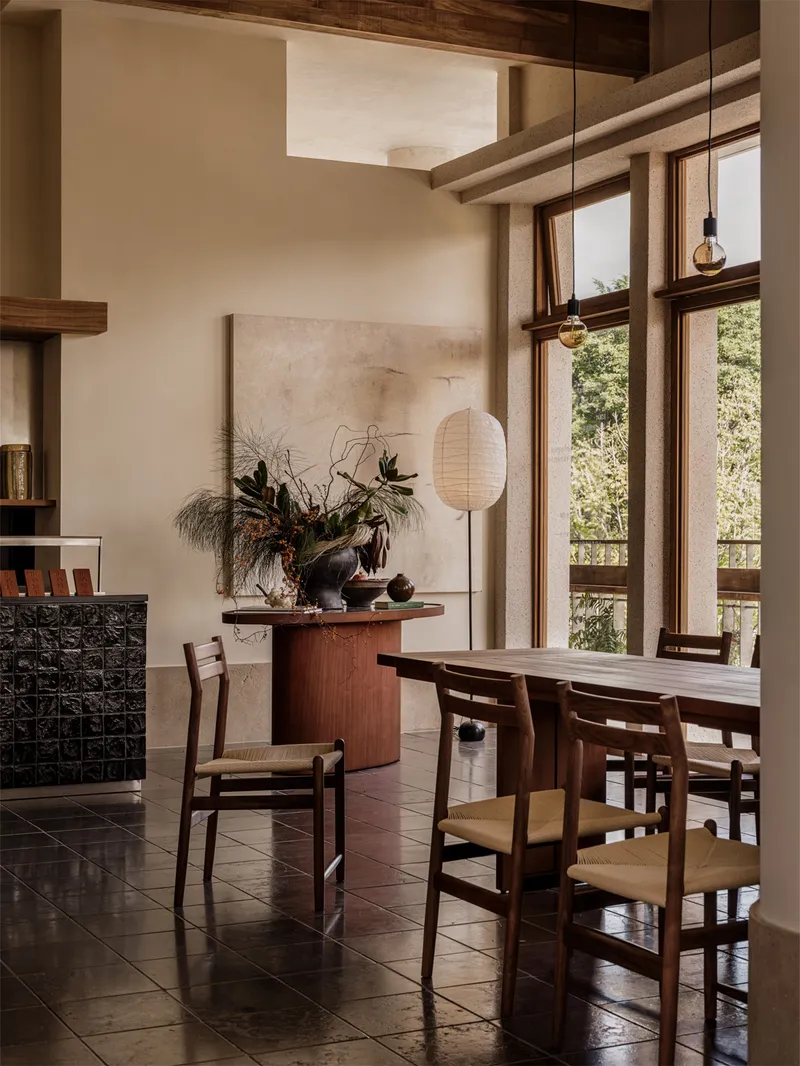 Double-height dining area with exposed timber beams and full-height glazing overlooking greenery