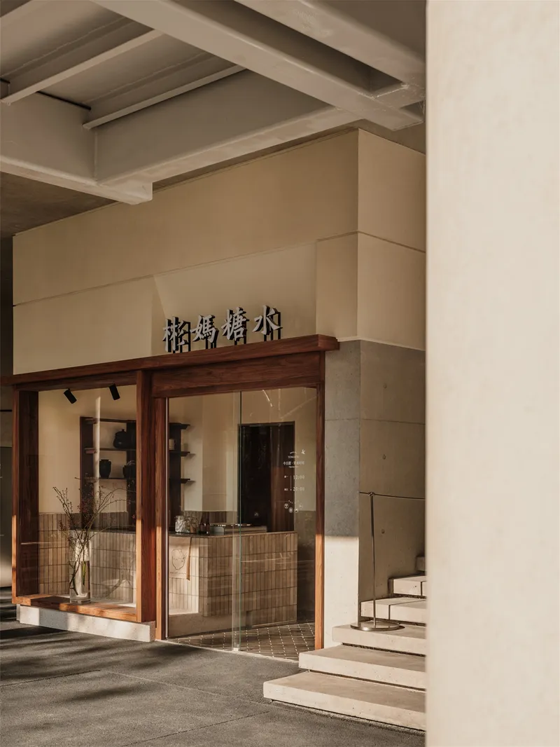 Storefront entrance with timber frame, tiled base, and stepped stone pavement under exposed concrete soffit