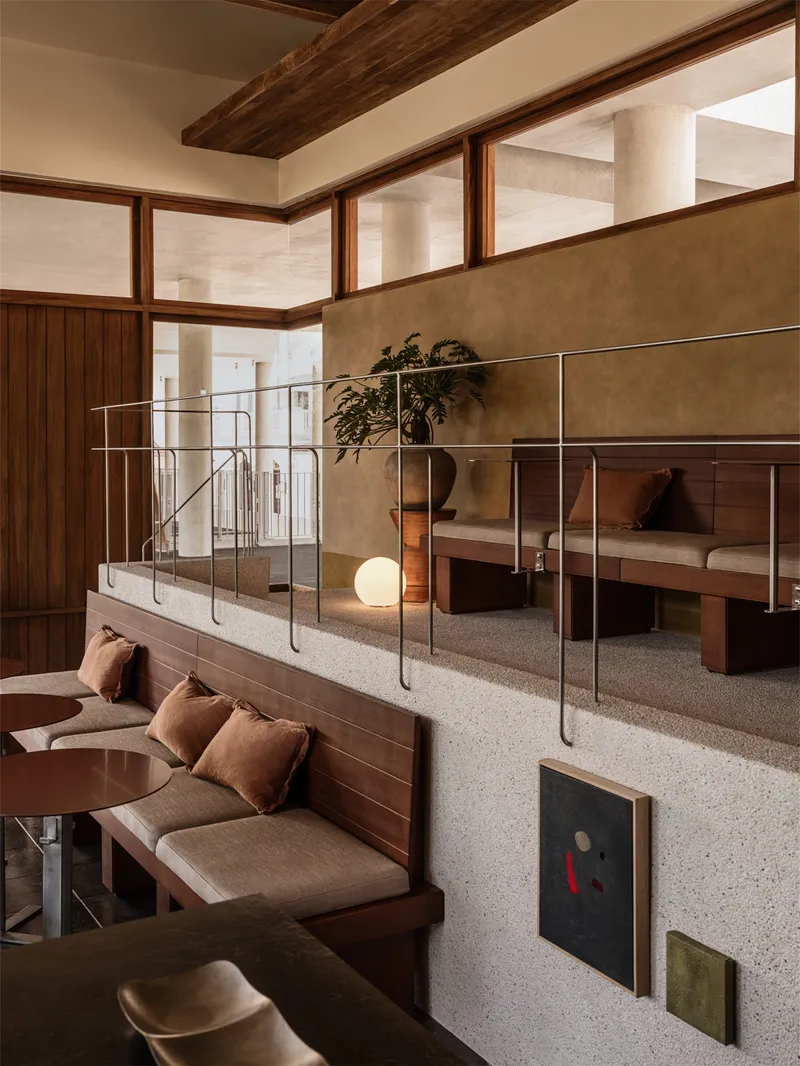 Split-level interior with terrazzo floor, timber-framed glazing, and exposed ceiling beams in warm afternoon light