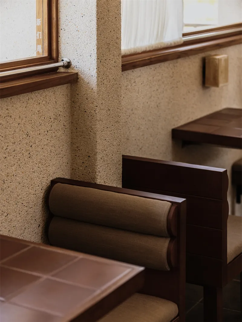 Timber window sill and terrazzo wall meeting a built-in bench with cylindrical bolster cushions