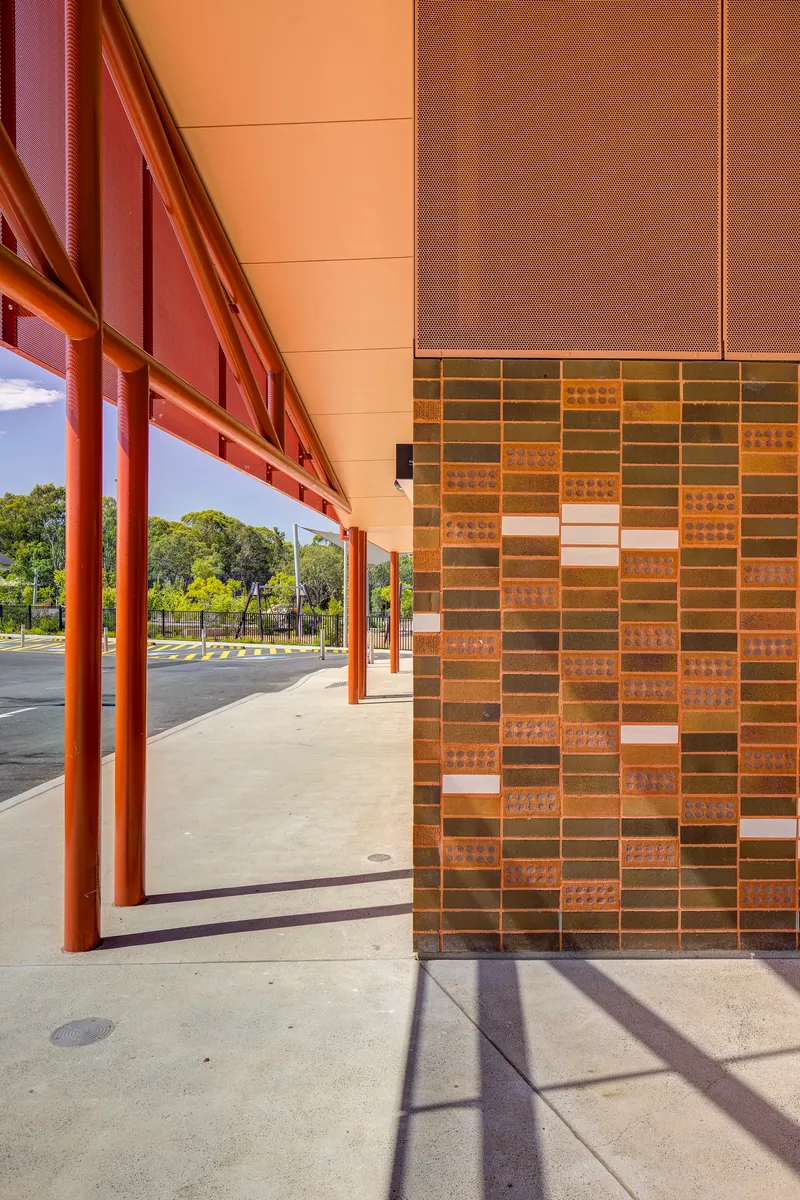 Brick column with variegated terracotta tiles beneath the deep overhang and red steel beams