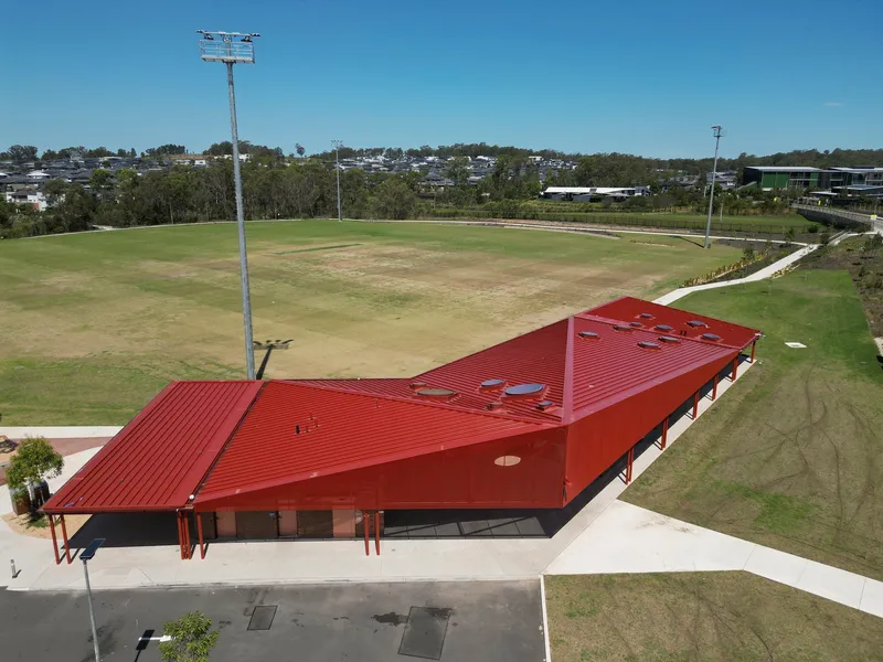 Aerial view of the angular red metal roof with service penetrations beside the oval field