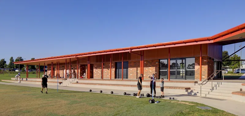 Covered veranda with slender steel columns and tiered concrete seating overlooking the playing field