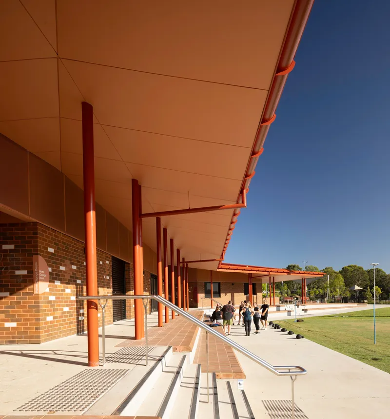Covered walkway with steel columns and cream ceiling panels alongside variegated brick facade in shadow