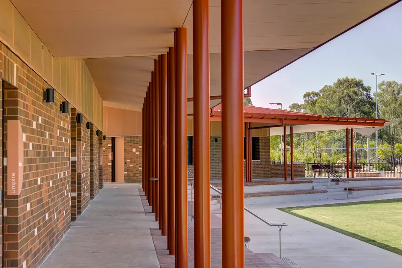 Covered walkway with reddish brown cylindrical columns along a multicolored brick wall under afternoon light