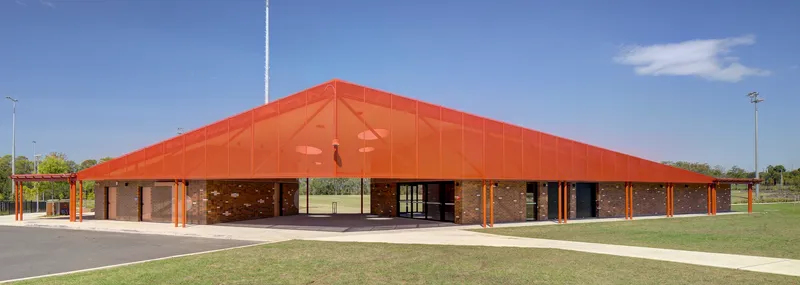 Wide low-pitched orange roof sheltering a brick colonnade under blue sky with scattered clouds